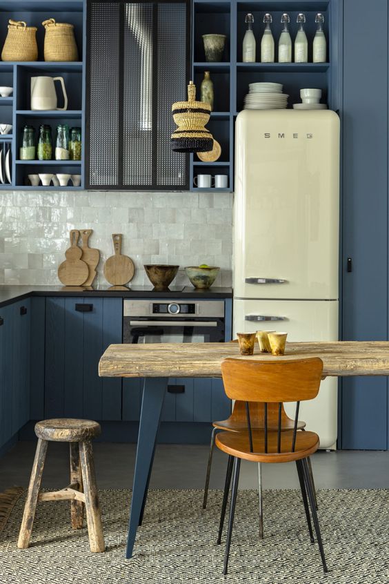 a beautiful and eye-catching kitchen with blue shiplap cabinets and open box ones, a grey tile backsplash, black countertops, a rough wood table