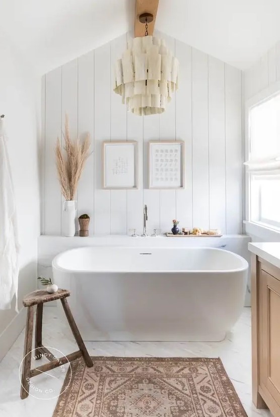a beautiful boho bathroom with an oval tub, a beadboard wall, a wooden vanity, a fabric chandelier is very chic