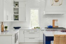 a beautiful coastal kitchen with white shaker cabinets, a bold blue kitchen island, white tiles and some bold blue touches