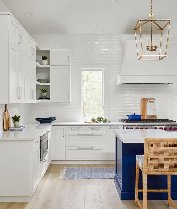 a beautiful coastal kitchen with white shaker cabinets, a bold blue kitchen island, white tiles and some bold blue touches