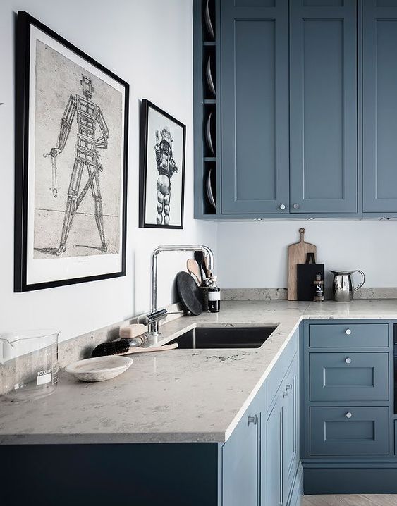 a beautiful kitchen with blue shaker style cabinets, grey sone countertops and eye-catching graphic artworks