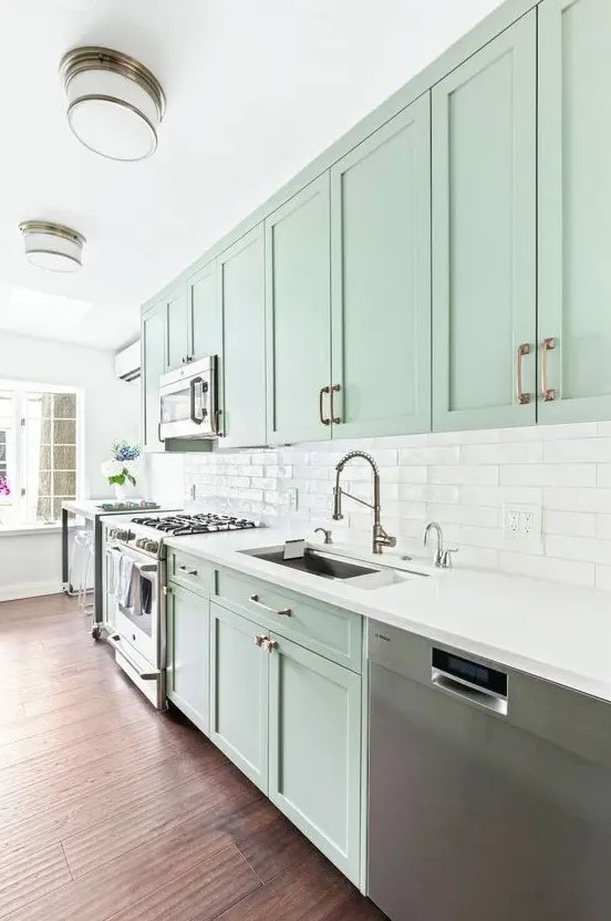 a beautiful mint green kitchen with shaker cabiners, a white tile backsplahs and white countertops, stainless steel appliances