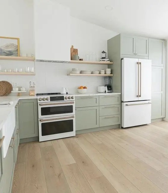 a beautiful sage green farmhouse kitchen with shaker cabinets, open shelves, a hood, a white cooker and brass fixtures