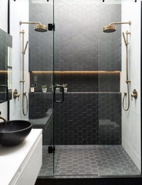 a black and white bathroom with black hex tiles and white tiles, a floating vanity with a black sink and brass fixtures