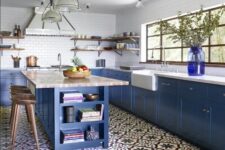 a blue farmhouse kitchen with a large kitchen island, stone countertops, white tile walls and a bold blue jar