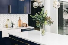 a bold and chic kitchen with navy cabinets, white countertops and a backsplash and a catchy chandelier with gold touches