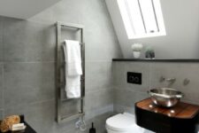 a bold attic bathroom with grey tiles, a black small vanity, a black clad tub and a white floor