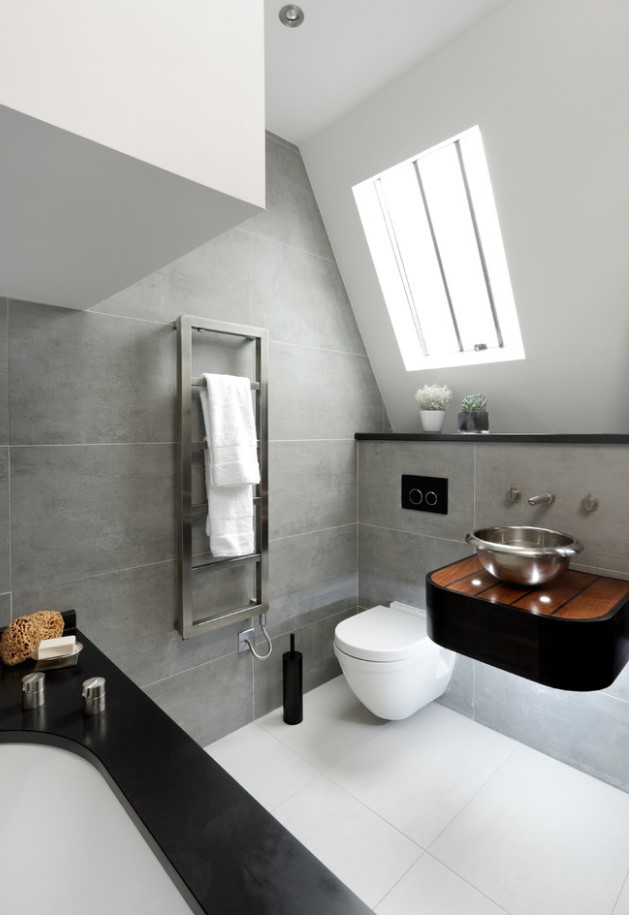 a bold attic bathroom with grey tiles, a black small vanity, a black clad tub and a white floor