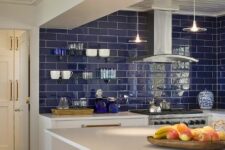 a bold kitchen with lower white cabinets, a bold blue tile backsplash, stainless steel appliances and pendant lamps