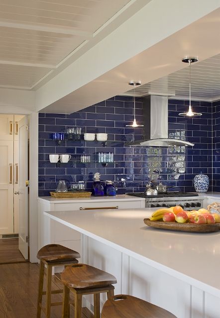 a bold kitchen with lower white cabinets, a bold blue tile backsplash, stainless steel appliances and pendant lamps
