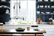 a bold kitchen with navy walls and matching open shelves, white lower cabinets, a stained dining set with benches and a unique lamp