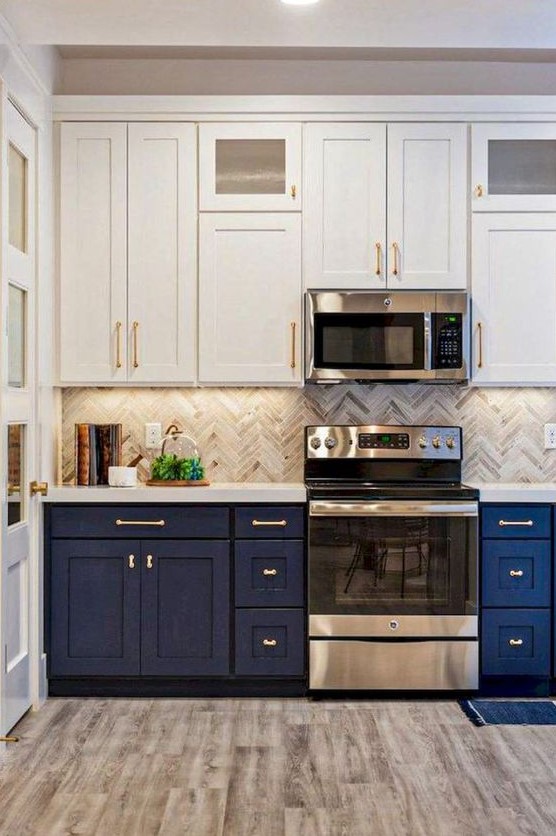 a bold two-tone kitchen with white and navy cabinets, a grey herringbone tile backsplash and white stone countertops