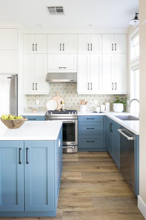 a breezy kitchen with pastel blue and white cabinets, a printed tile backsplash, white countertops, black handles