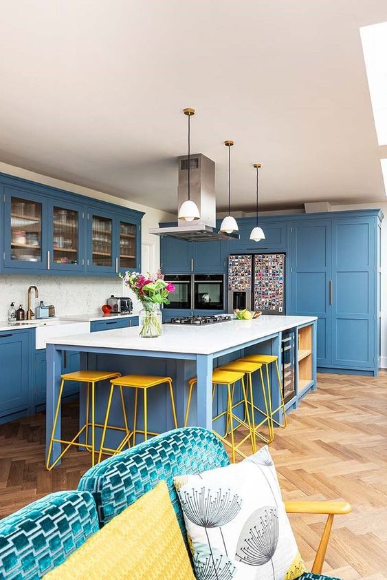 a bright and stylish coastal kitchen done in blue, with white countertops and a backsplash, pendant lamps and a sofa with pillows