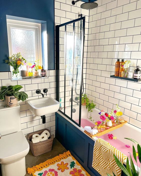a bright boho bathroom with navy panels and white subway tiles, a tub with shelves and bright blooms, colorful textiles