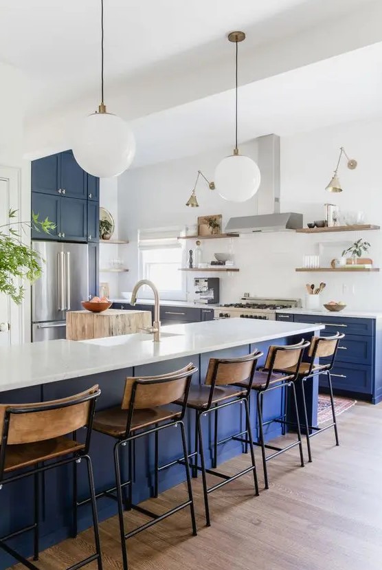 a bright kitchen with bold blue cabinets and a kitchen island, stained stools, shelves and pendant lamps plus sconces