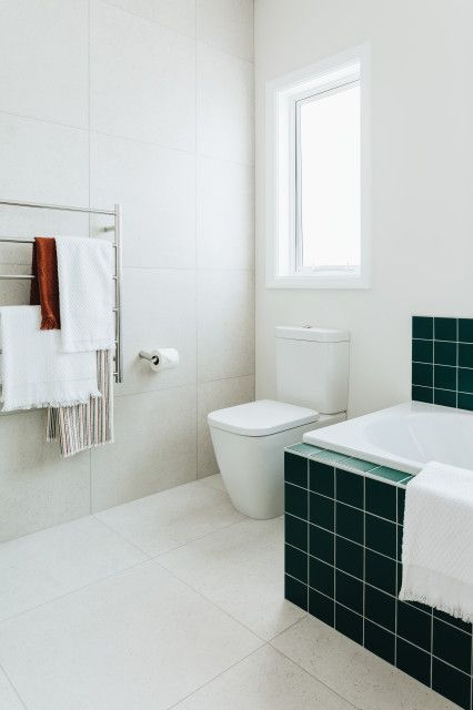 a catchy bathroom with neutral large format tiles and square green ones, white appliances and neutral textiles