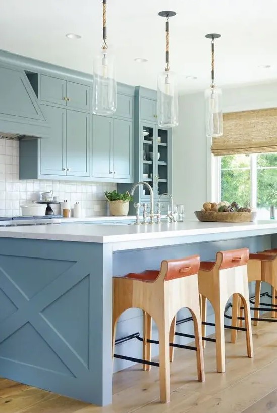 a chic coastal space with light blue cabinets, a blue kitchen island, glass pendant lamps and wood and leather stools