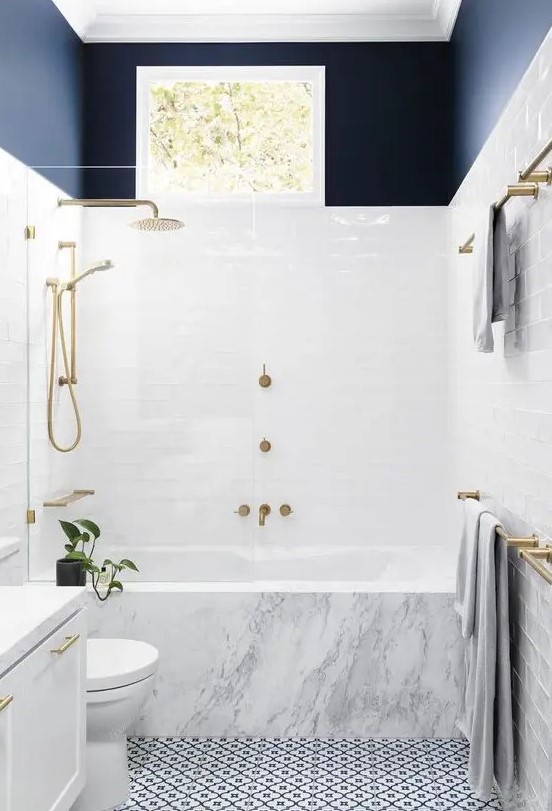 a chic contemporary bathroom with a mosaic floor, a marble clad tub, a navy toouch and gilded hardware