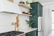 a chic kitchen with forest green and white cabinets, open shelves, gold and brass fixtures and some greenery