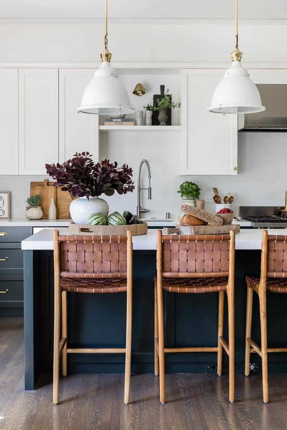 a chic kitchen with navy and white shaker style cabinets, a white backsplash, pendant lamps and woven stools