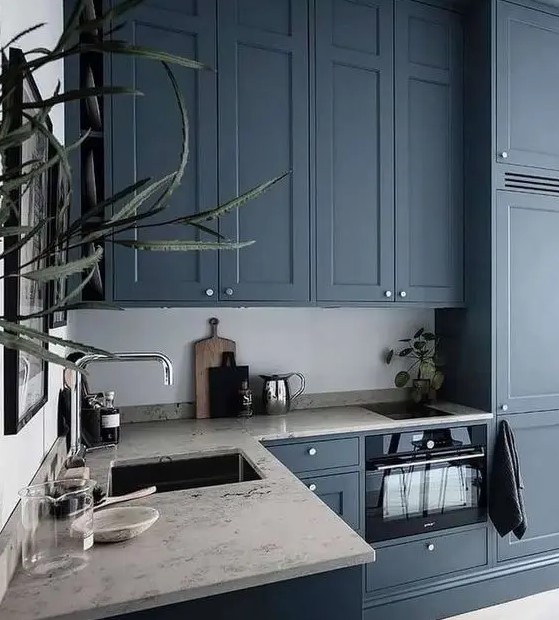 a chic kitchen with navy cabinets, neutral stone countertops, stainless steel fixtures and greenery