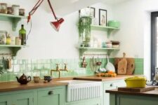 a chic mint green kitchen with shaker cabinets, butcherblock countertops, open shelves and a red sconce