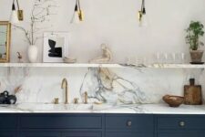 a chic navy kitchen with only lower cabinets, a marble countertop and backsplash, sconces and an open shelf