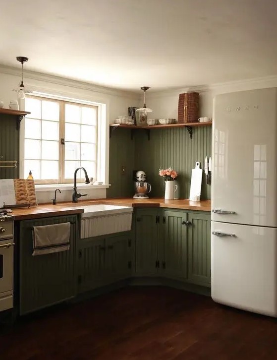 a chic olive green farmhouse kitchen with fluted cabinets, butcherblock countertops, black fixtures and open shelves is cool