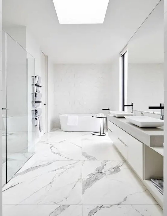 a chic white minimalist bathroom with marble large scale tiles, white furniture, white appliances and white hex tiles
