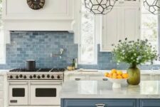 a classic sea-inspired kitchen with white shaker cabinets, a blue tile backsplash, a blue kitchen island with white stone countertops and beautiful faceted lamps