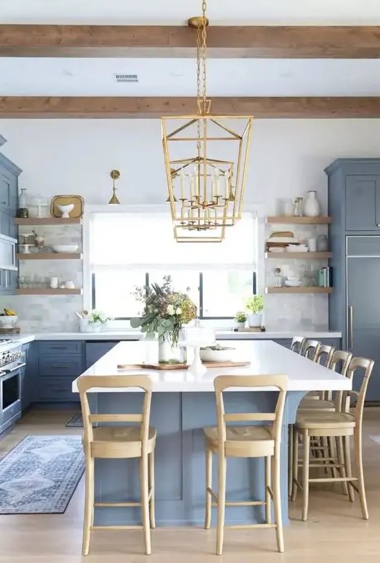 a coastal farmhouse kitchen with classic blue cabinetry and a kitchen island, wooden stools, beams and shelving and touches of gold