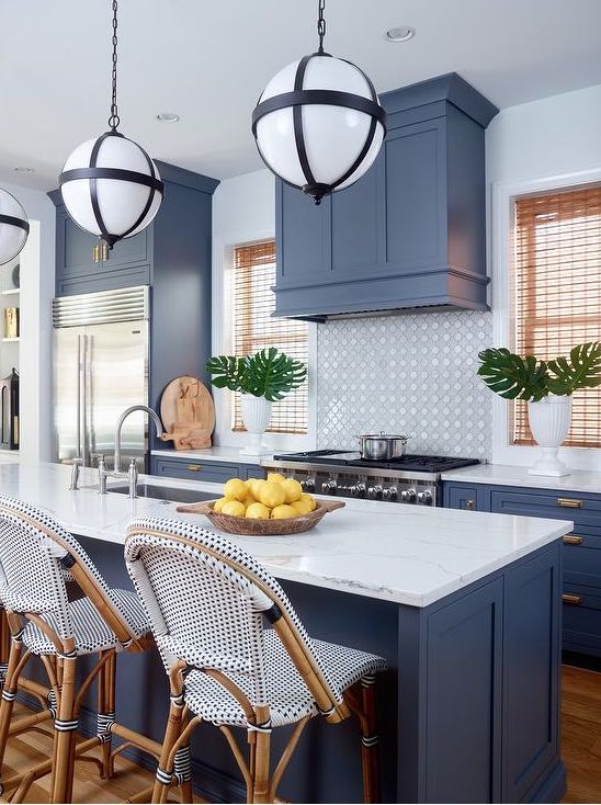 a coastal kitchen with blue shaker cabinets, white tiles, tall blue and white stools and cool pendant lamps on chain