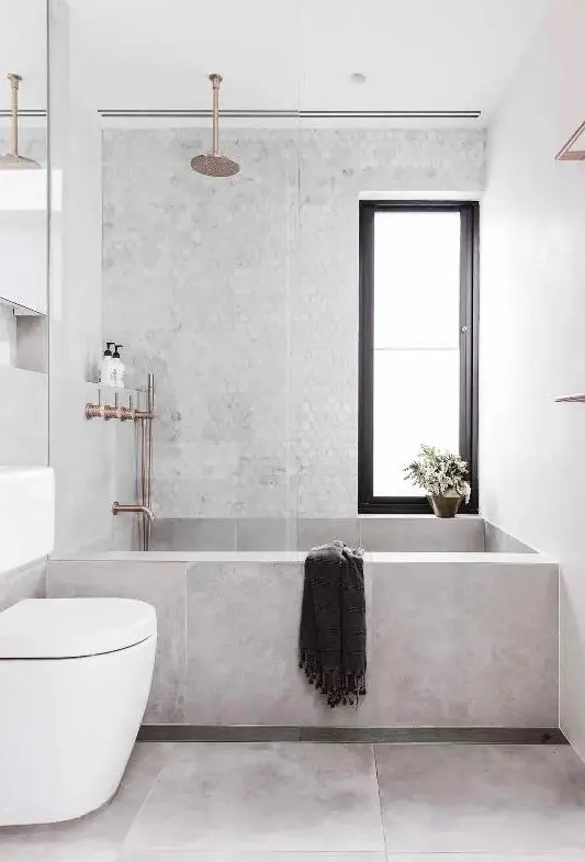 a contemporary bathroom clad with concrete and marble hex tiles, a tub clad with concrete tiles, white appliances and cropped fixtures