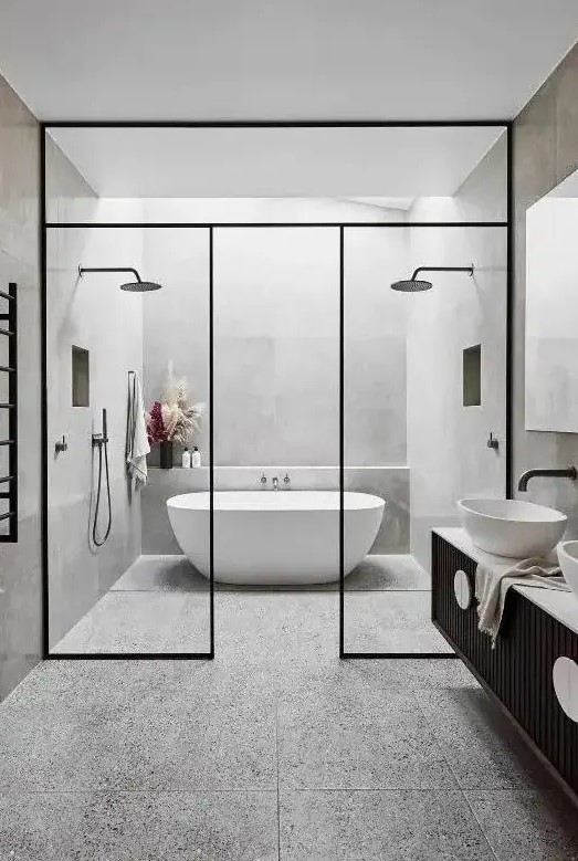 a contemporary bathroom clad with grey terrazzo tiles, a skylight over the tub, a black vanity and black framing, black fixtures