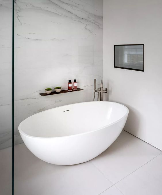 a contemporary bathroom with a marble wall and large format tiles, an oval tub, a shelf and a built-in fireplace