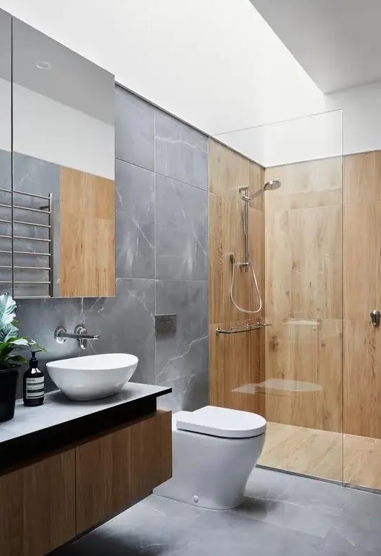 a contemporary bathroom with grey marble tiles and wooden paneling in the shower space, a floating vanity and a skylight