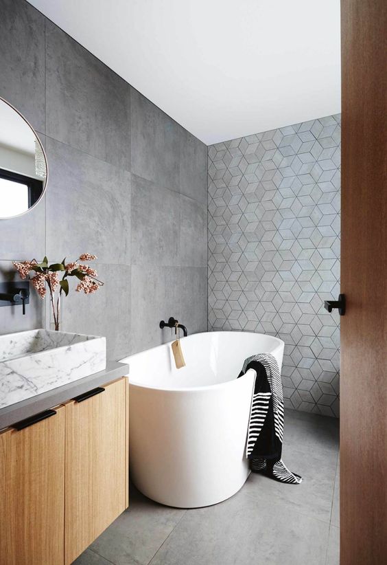 a contemporary bathroom with large format and geo tiles, a stained vanity, a marble sink, an oval tub and a round mirror
