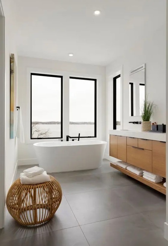 a contemporary bathroom with windows, large scale tiles, a timber vanity, a rattan pouf and some artwork