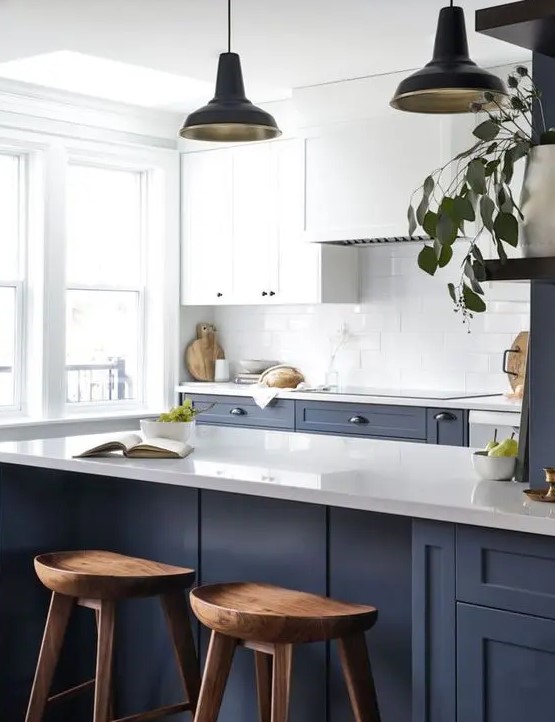 a contrasting kitchen with navy and white cabinets, a white tile backsplash, wooden stools and pendant lamps is a chic space