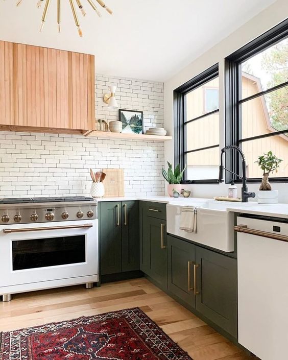 a cool kitchen with green cabinets, built-in appliances, a white brick backsplash and a stained wood hood