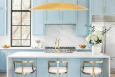 a delicate and chic kitchen with pastel blue shaker cabinets, a white marble backsplash, elegant tall stools and a large pendant lamp