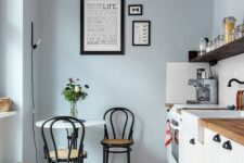a delicate pale blue kitchen with white shiplap cabinets, an open shelf, a small table and black chairs