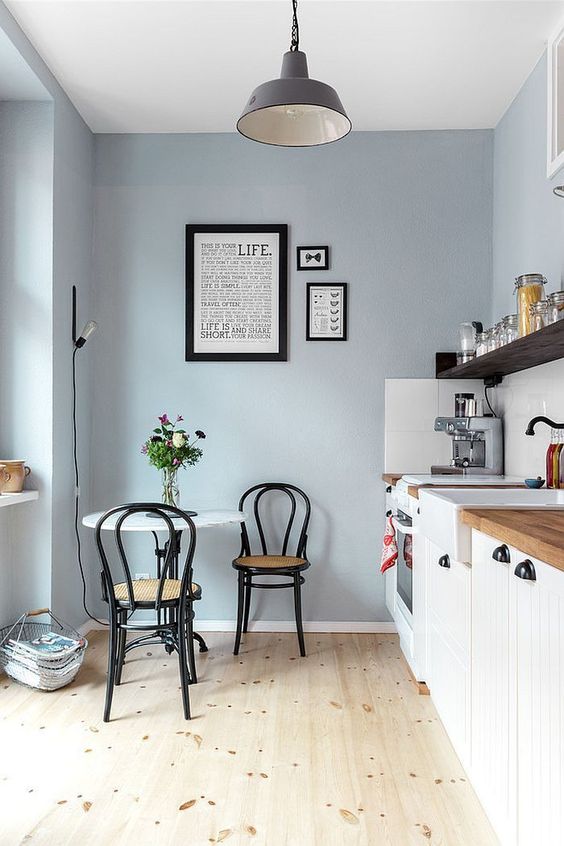 a delicate pale blue kitchen with white shiplap cabinets, an open shelf, a small table and black chairs