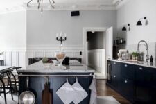 a dove grey Scandinavian kitchen with navy cabinets and a kitchen island, grey stone countertops, black sconces and a cool chandelier