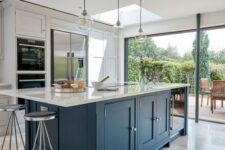 a dove grey kitchen with a large navy kitchen island and white stone countertops plus vintage stools and pendant lamps