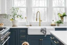 a farmhouse kitchen with white subway tiles, navy shaker cabinets, white countertops and potted plants