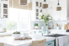 a gorgeous beach kitchen with white shaker cabinets, a geo tile backsplash, woven blinds, a light blue kitchen island and woven stools plus glass lamps with burlap touches