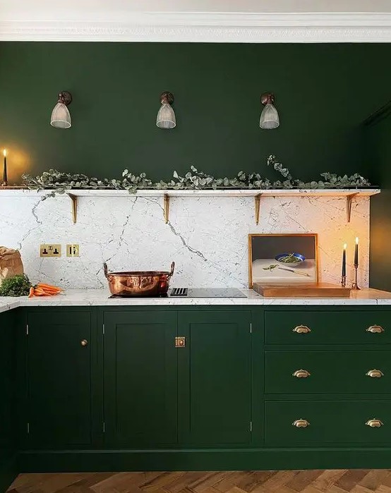 a hunter green kitchen with vintage cabinets, gold handles, an open shelf with greenery and a white stone backsplash