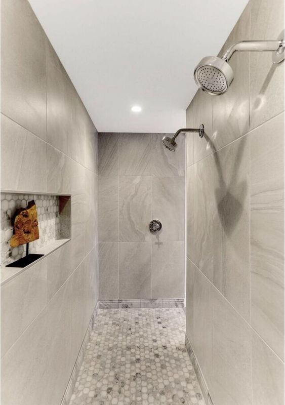 a large shower space with large format tiles and hexagon ones on the floor plus a niche for storage and decor